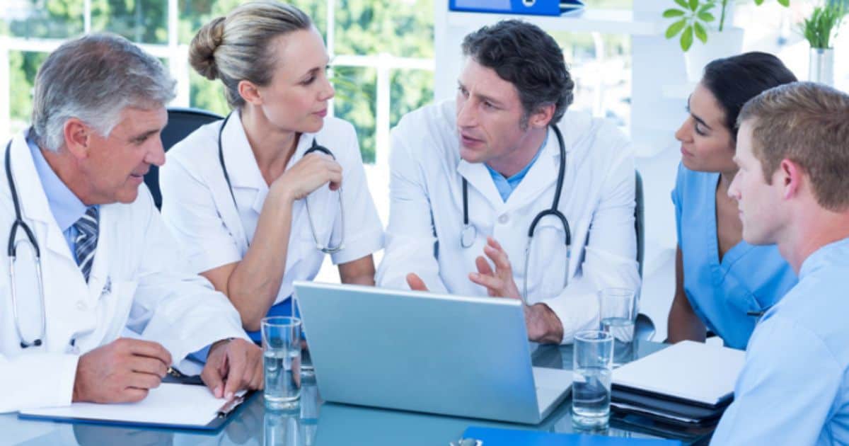 A team of surgeons sit around a computer discussing how surgical skill impacts patient outcomes.